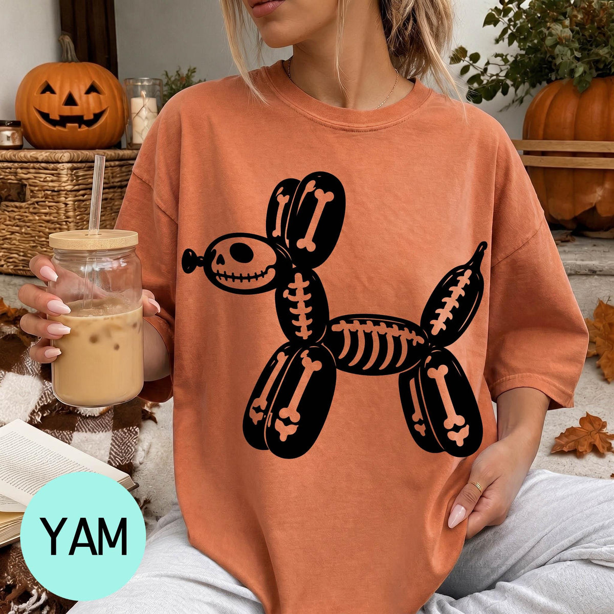 A woman wearing an orange t-shirt with a skeleton dog graphic is sitting on a couch, holding a drink in a glass.