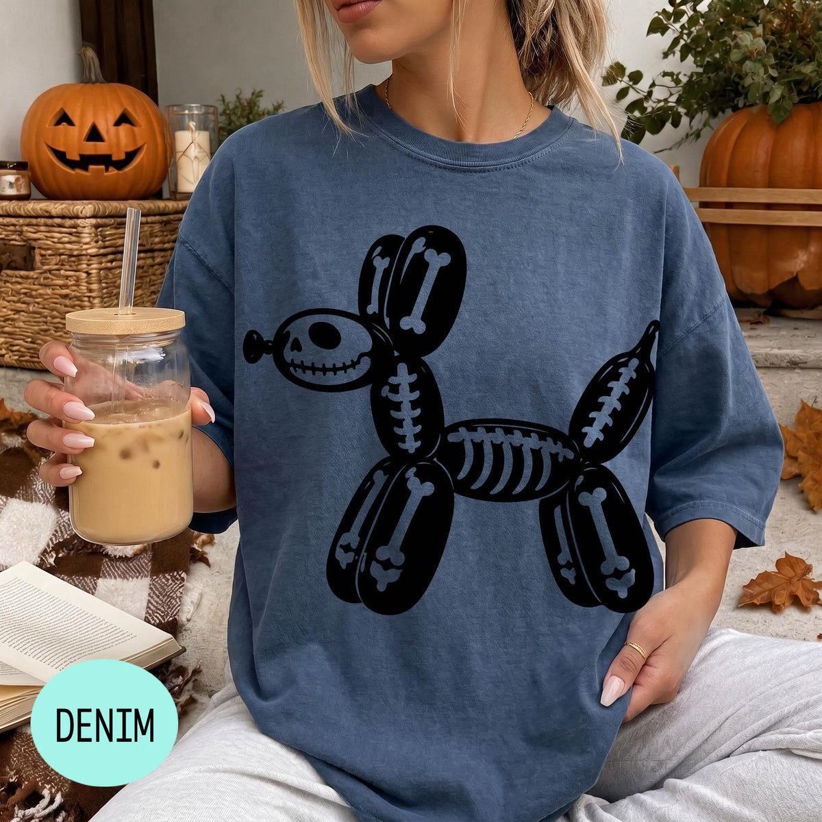 A woman wearing a blue t-shirt with a skeleton dog graphic is sitting on a couch, holding a drink in a glass with a straw.