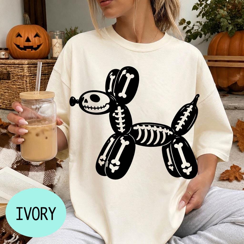 A woman wearing a white t-shirt with a skeleton dog graphic is sitting on a couch, holding a glass of iced coffee.