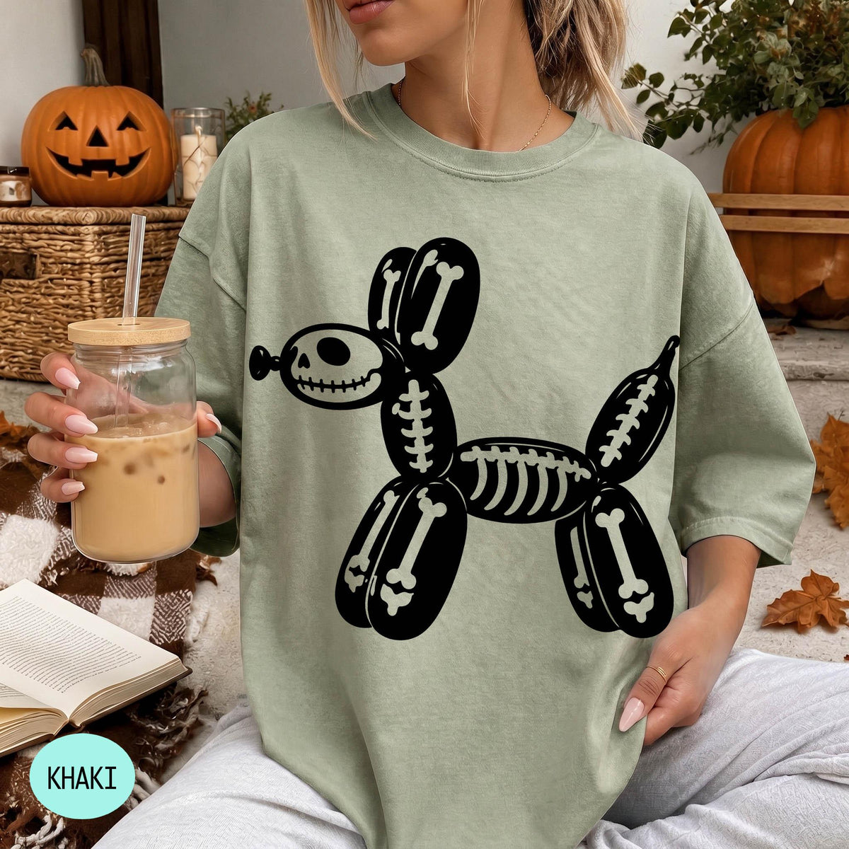 A woman wearing a green t-shirt with a skeleton dog graphic is sitting on a couch, holding a glass of iced coffee.