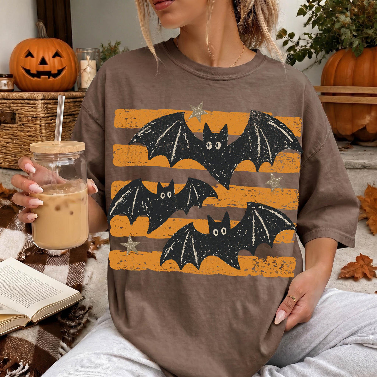 A woman is sitting on a couch, wearing a t-shirt with a graphic of bats and stars, holding a drink in a glass.