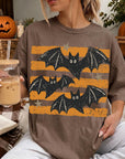 A woman is sitting on a couch, wearing a t-shirt with a graphic of bats and stars, holding a drink in a glass.